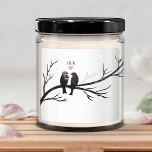 May include: A white candle with a black lid and a label that says "J&K" with a pink heart and two birds on a branch with the word "love" written in pink.