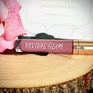 May include: A pink lip gloss tube with a gold cap. The tube has the words "REVIVAL GLAM" printed on it.