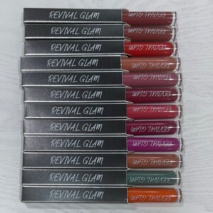 May include: A set of 12 silver lipstick tubes with the words "Revival Glam" printed on the front and "REVIVAL GLAM" printed on the back. The lipsticks are in various shades of red, pink, purple, brown, green, and orange.