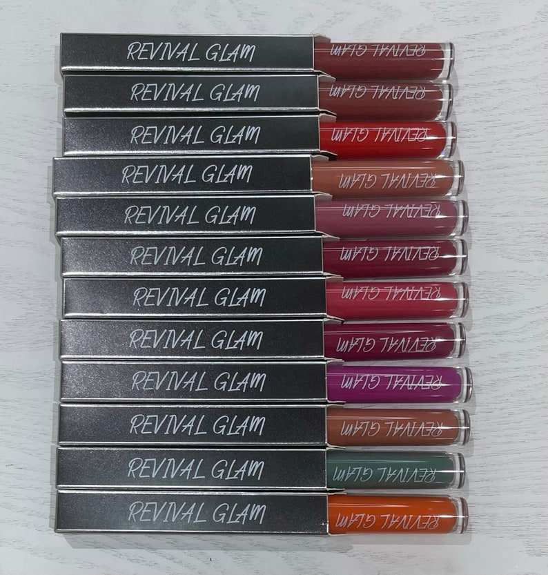 May include: A set of 12 silver lipstick tubes with the words "Revival Glam" printed on the front and "REVIVAL GLAM" printed on the back. The lipsticks are in various shades of red, pink, purple, brown, green, and orange.