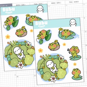 May include: Two sticker sheets featuring cute frog and character illustrations. The stickers include frogs on lily pads, flowers, and a character in a lily pad. The text "Bubu Studio" is visible on the stickers. The background is a calendar.