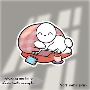 Puede incluir: Una pegatina de vinilo troquelada que representa una figura de dibujos animados relajándose en una almohada con un libro, una tableta y café. La pegatina tiene el texto "relaxing me time" y "die cut vinyl". La pegatina tiene un acabado mate suave.