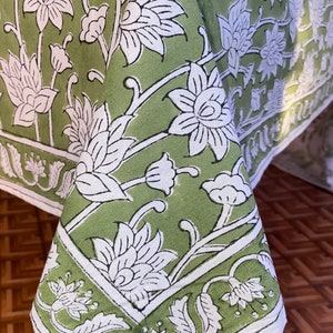 May include: Green tablecloth with a white floral pattern. The tablecloth has a border with a white floral design.