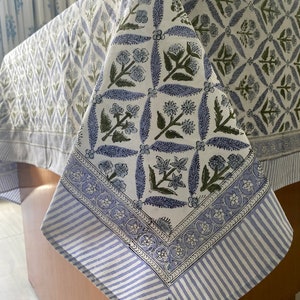 May include: A white tablecloth with a blue and green floral pattern. The tablecloth has a striped border.