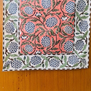 May include: A pink and white table runner with a floral pattern featuring blue and green leaves and flowers. The pattern is repeated in a border around the edges of the runner.
