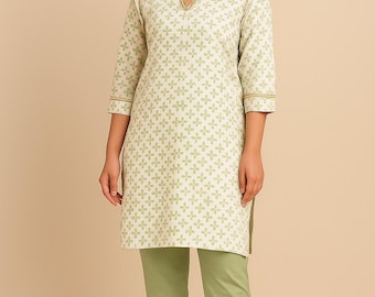 May include: A two-piece outfit featuring a cream-colored tunic with a green floral pattern and three-quarter sleeves. The tunic has gold trim around the neckline and sleeves. The outfit includes matching green pants. The model is wearing brown sandals.