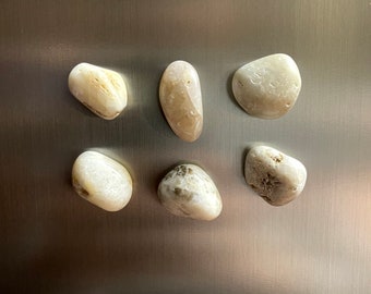 May include: Six smooth, white and brown stones with a mottled pattern. The stones are arranged in a grid pattern on a silver surface.
