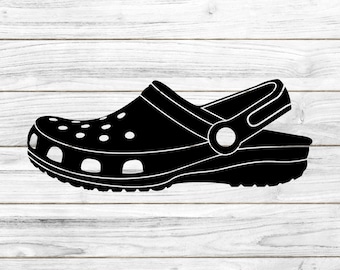 May include: Black silhouette of a clog shoe with a strap on the back. The shoe has a textured sole and a round hole on the strap.