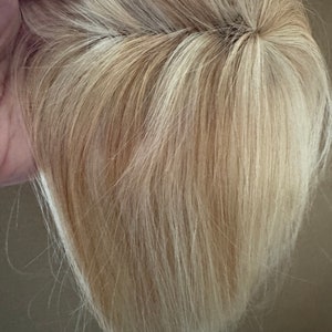 May include: A blonde human hair topper with a natural-looking parting. The hair is straight and appears to be in good condition.