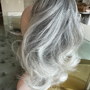 Könnte beinhalten: Eine lange, wellige Haarverlängerung in Grau und Weiß. Das Haar ist in lockeren Wellen gestylt und hat einen natürlichen, verlaufenden Look.