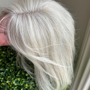 Op de afbeelding: Een lange, rechte, witte pruik met een kantfront. De pruik is in een eenvoudige, natuurlijke stijl gestyled.