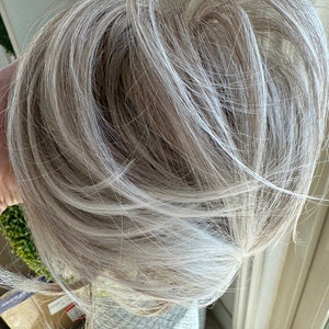 May include: A close-up of a light blonde ponytail with white highlights. The hair is pulled back and tied with a hair tie.
