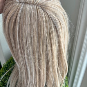 Op de afbeelding: Een close-up van een lichtblond pruik met een rechte, gladde stijl. De pruik heeft een natuurlijk ogende scheiding en een zachte, zijdeachtige textuur.