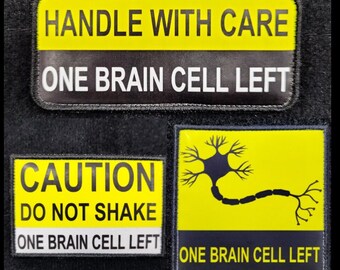 May include: Three yellow warning signs with black text and a black neuron illustration. The signs read "Handle with care, One brain cell left", "Caution, Do not shake, One brain cell left", and "One brain cell left".