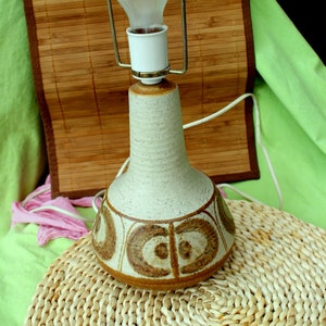 Op de afbeelding: Een keramische tafellamp met een witte en bruine gepatroneerde basis. De lamp heeft een heldere glazen kap en een gloeilamp.