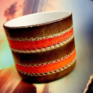Könnte beinhalten: Eine braune Keramiktasse mit orangefarbenen und weißen Streifen. Die Tasse hat eine strukturierte Oberfläche und ein weißes Inneres.