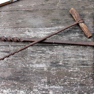 May include: Two antique hand-cranked wood augers with wooden handles, lying on a weathered wooden surface.