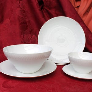 May include: A white porcelain dinnerware set consisting of two bowls and three plates. The pieces feature a subtle, embossed geometric pattern around the rims. The set includes one large bowl, one small bowl, and three matching circular plates.