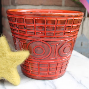 Könnte beinhalten: Ein roter Keramiktopf mit einer Waffelstruktur und dem Wort "TOTO" in Relief auf der Seite.