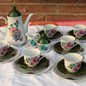 Könnte beinhalten: Ein Vintage-Blumenservice mit einer grün-weißen Teekanne, Zuckerdose, Milchkännchen und sechs Tassen und Untertassen. Die Tassen und Untertassen haben ein Blumenmuster mit rosa, grünen und blauen Blumen.