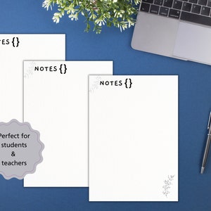 K&ouml;nnte beinhalten: Drei wei&szlig;e Notizbl&ouml;cke mit dem Text "NOTES {}" auf jedem. Die Notizbl&ouml;cke liegen auf einer blauen Oberfl&auml;che mit einem Laptop, einem Stift und einem Notizbuch im Hintergrund.