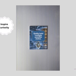 Pu&ograve; includere: Un poster rettangolare con sfondo blu, un piccolo robot e il testo Qubits hold multiple possible states. A sinistra, un badge bianco smerlato riporta il testo Inspire curiosity. Il poster &egrave; posizionato su uno sfondo di colore argento.