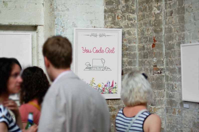 May include: A white framed poster with the text "You Code Girl" in pink lettering. The poster features a line drawing of a computer with a hat on top of it, a keyboard, and a mouse. The poster is surrounded by a border of flowers.