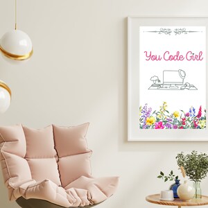 May include: A white framed print featuring a black and white line drawing of a computer desk with a laptop, a plant, and a hat on top of the laptop. The text "You Code Girl" is in pink lettering above the drawing. The bottom of the print has a border of watercolour flowers in various colours.