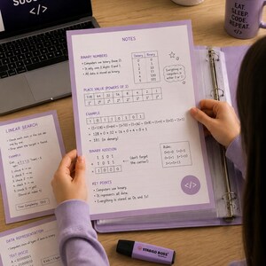 Pode incluir: Um fichário roxo claro contendo folhas de estudo educativas sobre números binários, valores posicionais e representação de dados. As páginas apresentam texto impresso, tabelas e diagramas de ciência da computação, junto a um marcador roxo.