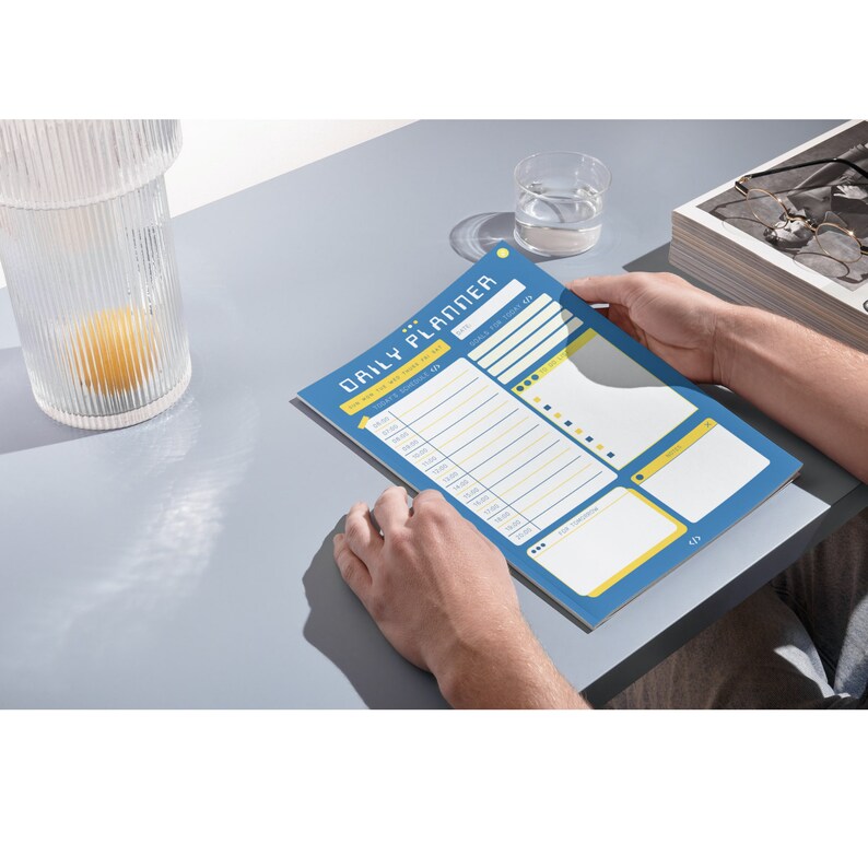 Peut inclure: Un agenda quotidien bleu et jaune avec le texte "DAILY PLANNER" en haut. L'agenda comporte des sections pour les objectifs, la liste des choses &agrave; faire et un horaire.