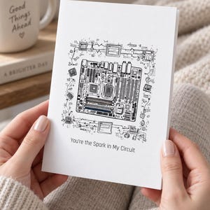 May include: A white greeting card featuring a detailed black ink illustration of a computer motherboard surrounded by smaller electronic components and circuitry. The text below the illustration reads, You're the Spark in My Circuit.