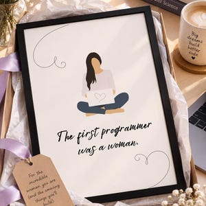 Puede incluir: Una impresión enmarcada en una caja de regalo con una figura de cabello negro sentada con las piernas cruzadas y un portátil. El texto dice, The first programmer was a woman. Una etiqueta de papel marrón dice, For the incredible woman you are (and the amazing things you'll build).