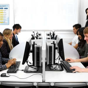 Puede incluir: Un aula con estudiantes trabajando en ordenadores. Un cartel titulado "Python Basics" est&aacute; expuesto en la pared. Los estudiantes est&aacute;n sentados en estaciones de trabajo individuales con monitores de ordenador negros y teclados.