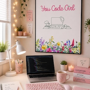 May include: A framed wall art print featuring the text You Code Girl in pink script above a line drawing of a computer desk, with a colorful floral border at the bottom. The print is displayed in a workspace with a laptop, pink keyboard, and books.