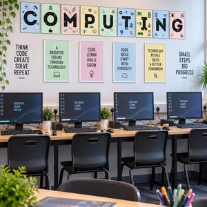 May include: A computer lab featuring four workstations with monitors displaying "DISCOVER LEARN CREATE". The wall displays the word "COMPUTING" in individual frames, motivational text posters, and a stack of books titled "Computer Science".