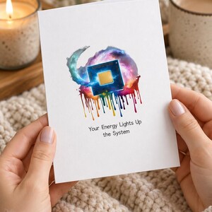 May include: A white greeting card featuring a central illustration of a blue computer processor surrounded by a colorful nebula and paint drips in rainbow hues. Below the graphic, the text reads: Your Energy Lights Up the System.
