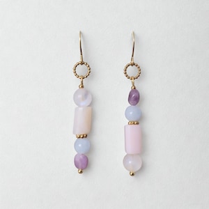 Peut inclure: Paire de boucles d'oreilles pendantes avec crochets dorés et perles pastel. Chaque boucle d'oreille est composée de perles roses, lavande et bleues, avec une petite perle dorée en bas. Bijoux pour oreilles percées.