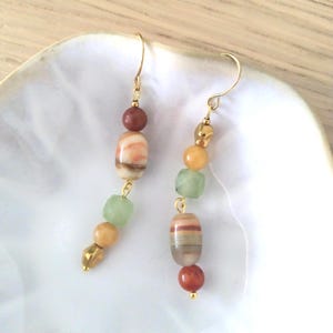 May include: A pair of drop earrings featuring gold-tone hooks and a vertical arrangement of beads. Each earring includes a mix of round and faceted beads in shades of terracotta, cream, pale yellow, and light green, connected by gold-tone wire.