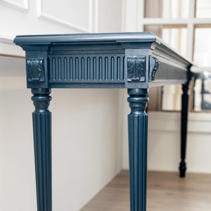 Könnte beinhalten: Eine marineblaue Konsolentisch mit aufwendigen Details. Der Tisch hat geschnitzte florale Akzente und vertikale Rillen. Die Beine sind geriffelt und der Tisch hat ein langes, schmales Design. Der Tisch ist aus Holz.
