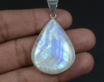 May include: A teardrop-shaped moonstone pendant featuring a smooth, polished surface with iridescent blue and white flashes. The gemstone is set in a simple silver-toned metal frame with a triangular bail at the top for attaching to a necklace chain.