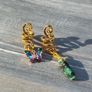 Puede incluir: Dos pendientes de oreja de oro con un diseño en espiral. Un pendiente tiene un dije de mariposa iridiscente y el otro tiene un dije de piedra preciosa verde.