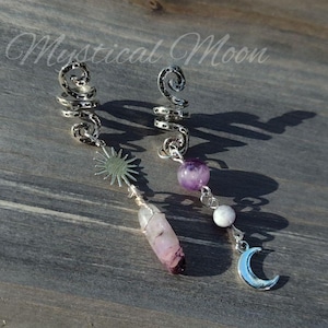 May include: Two silver hair cuffs with dangling charms. One charm features a silver sun, a purple and white crystal, and a silver crescent moon. The other charm features a purple crystal and a white bead.
