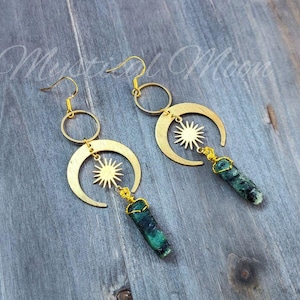 May include: Gold crescent moon earrings with a sun charm and a green gemstone dangle.