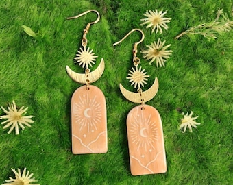 Orecchini pendenti con luna crescente e raggi di sole dorati, gioielli boho celestiali con ciondoli ad arco beige incisi e design a stella e luna.