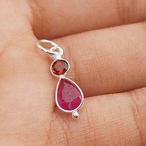 May include: A silver pendant with a teardrop-shaped red gemstone and a smaller round red gemstone.