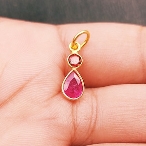May include: A gold pendant featuring a teardrop-shaped ruby gemstone and a smaller round ruby gemstone.