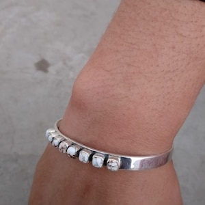 May include: A silver bracelet with white stones set in a row. The bracelet is on a person's wrist.