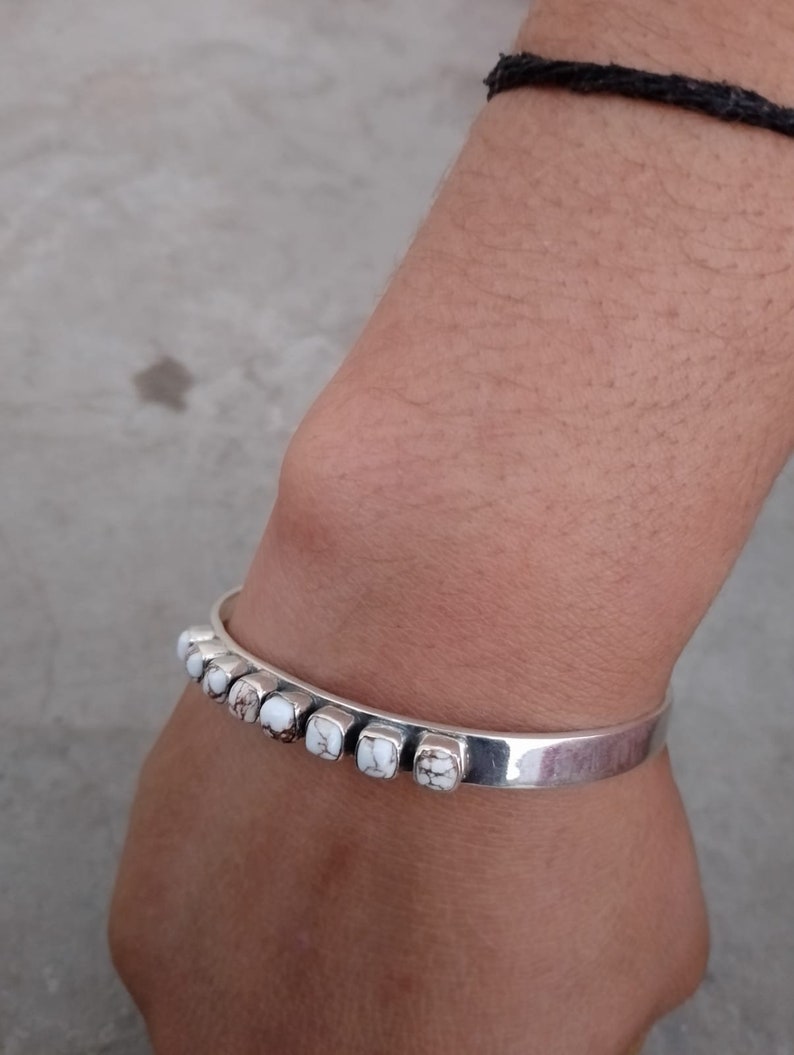 May include: A silver bracelet with white stones set in a row. The bracelet is on a person's wrist.