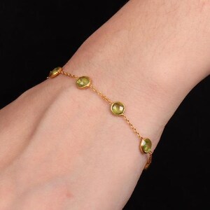 May include: A delicate gold bracelet featuring a series of round, light green gemstones. The bracelet is worn on a wrist, showcasing the jewelry's design and color against the skin. The gemstones are evenly spaced along the gold chain.