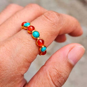 May include: A gold band ring featuring a series of alternating round, smooth cabochon stones in vibrant turquoise blue and deep orange-red colors, set in a continuous row along the top of the metal band.
